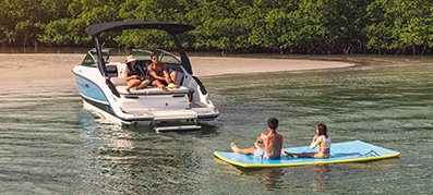 A white and blue Sea Ray Boat sits anchored at a sandy island with children playing in the water