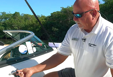 A man in a white polo shirt tying a knot onto a boat on a sunny day with trees in the background