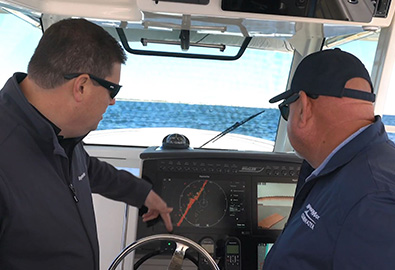 Two men looking at the navigation screen on a boat, as it shows a red diagonal line across the middle.