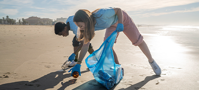 Two individuals helping to clean up trash along the beach